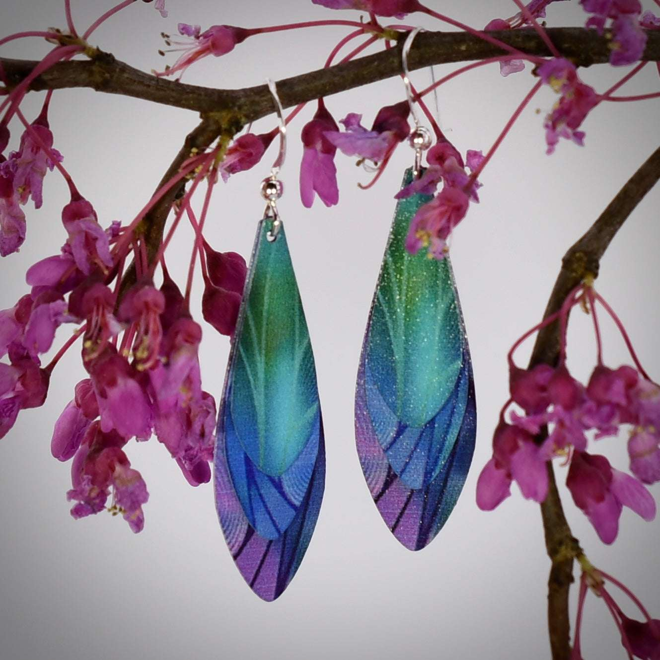 Layered stainless steel feather earrings in iridescent blue, green, and purple, with hypoallergenic sterling silver ear wires.