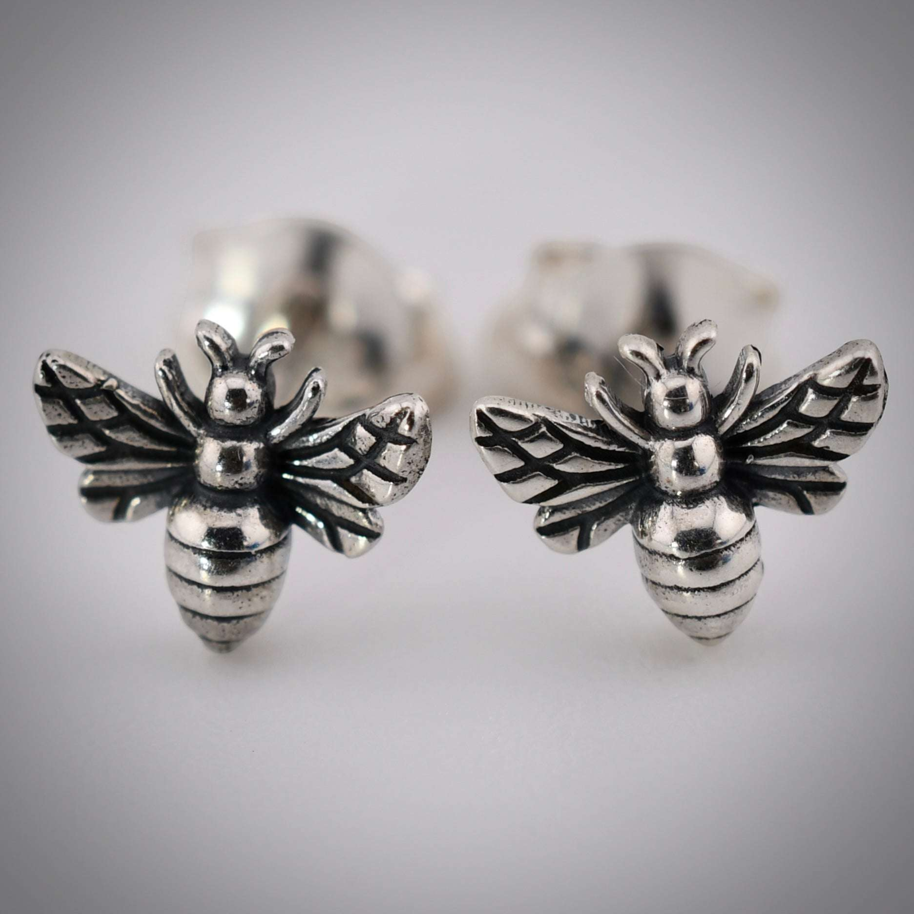 Dainty recycled sterling silver post earrings shaped like tiny bees with detailed wings and segmented bodies.
