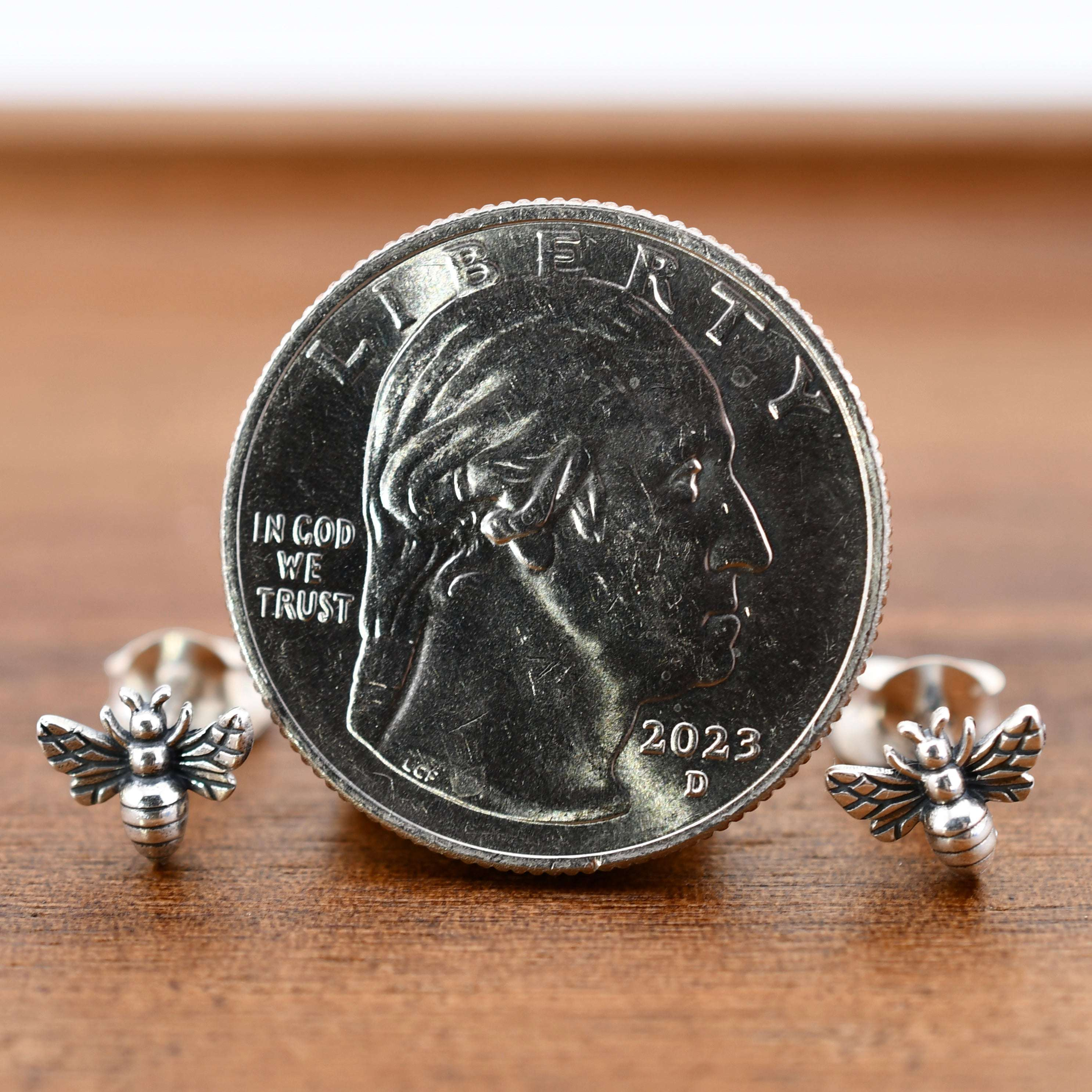 Tiny recycled sterling silver bee stud earrings with detailed wings and segmented bodies, shown next to a quarter for scale.